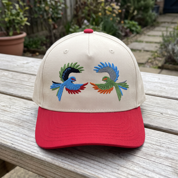Colorful Tropical Bird embroidered hat in Red/natural resting on a flat surface