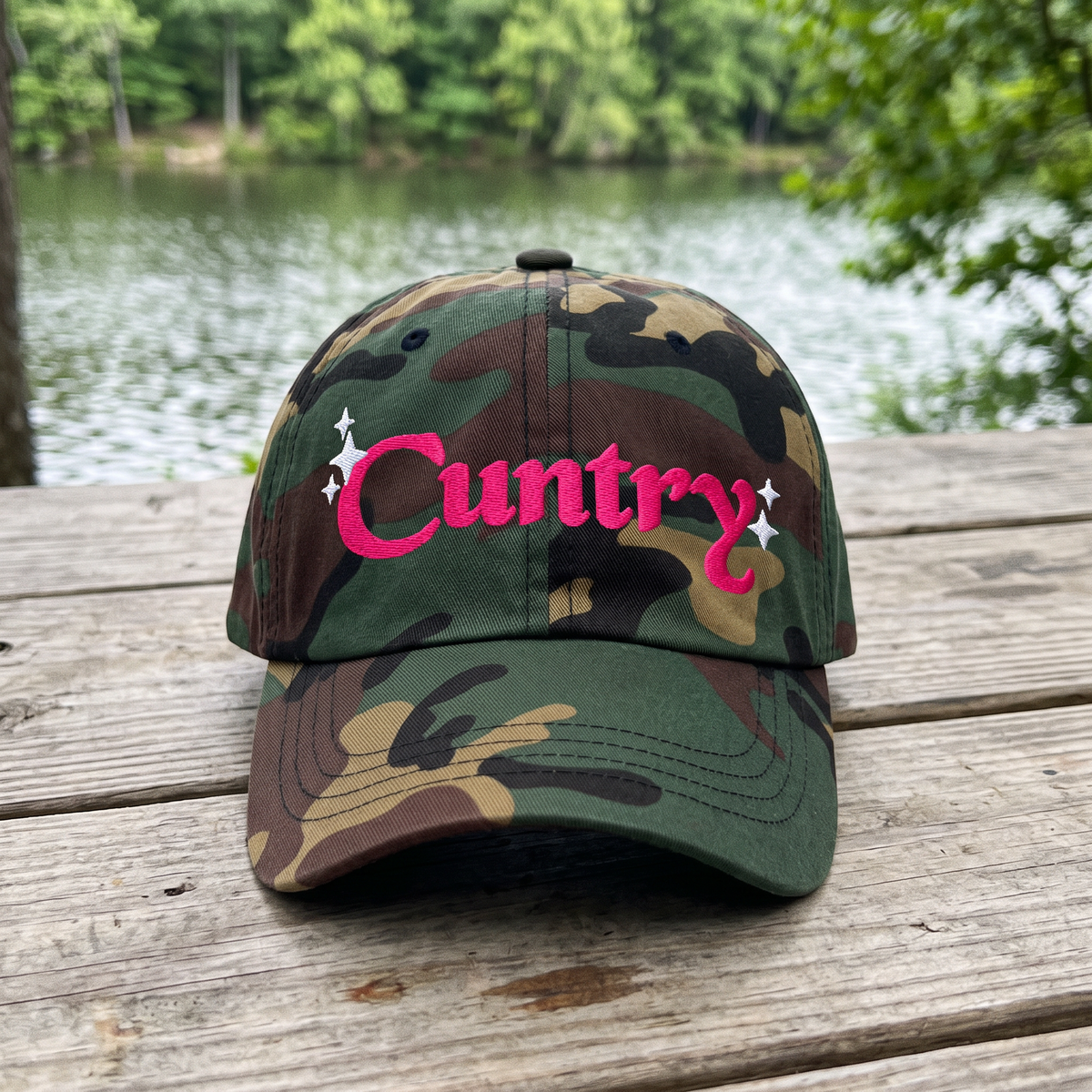 Country Word Art embroidered hat in Green Camo resting on a flat surface, lifestyle image 1