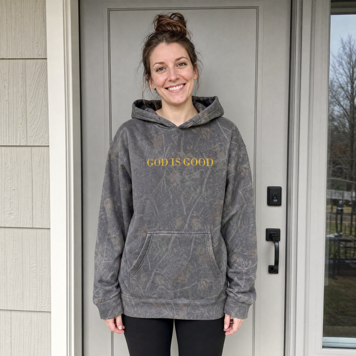 Model wearing the God Is Good heavyweight hoodie in Darkwood Tree Camo, lifestyle image 1