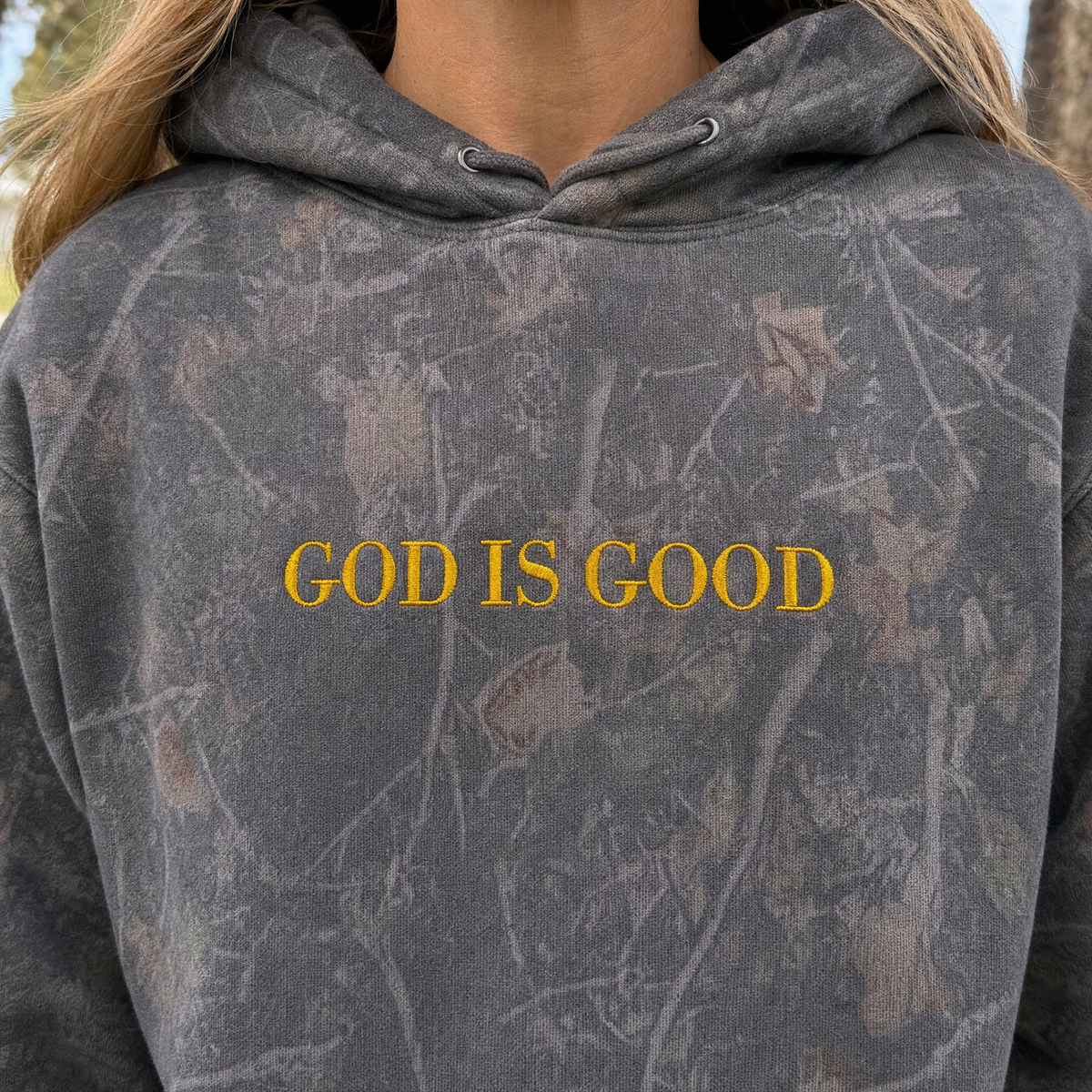 Model wearing the God Is Good heavyweight hoodie in Darkwood Tree Camo, lifestyle image 2