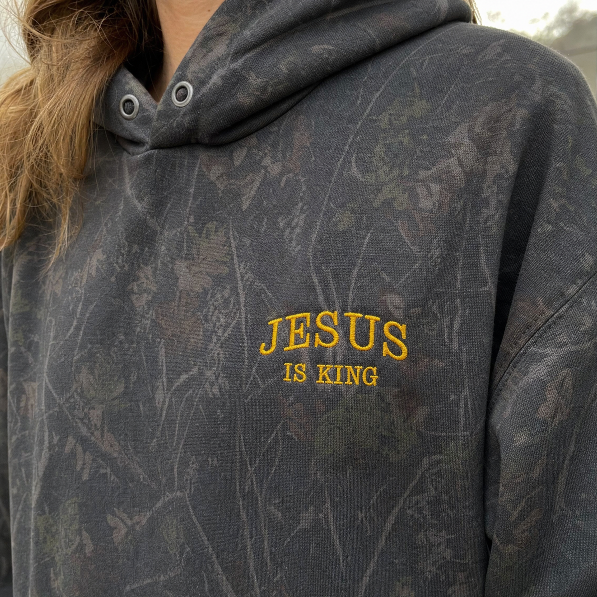 Model wearing the Jesus Is King heavyweight hoodie in Darkwood Tree Camo, lifestyle image 2