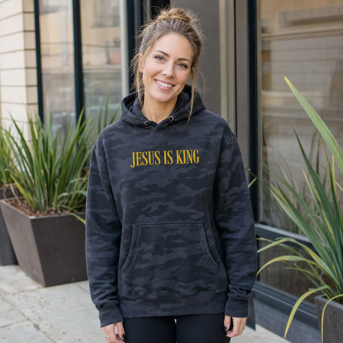 Model wearing the Jesus Is King heavyweight hoodie in Black Camo, lifestyle image 1