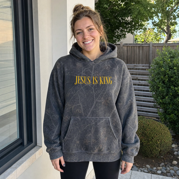 Model wearing the Jesus Is King heavyweight hoodie in Dark Tree Camo, cover image 1