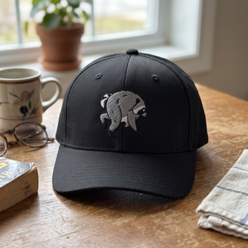 Jimothy Raccoon embroidered hat in Black resting on a flat surface