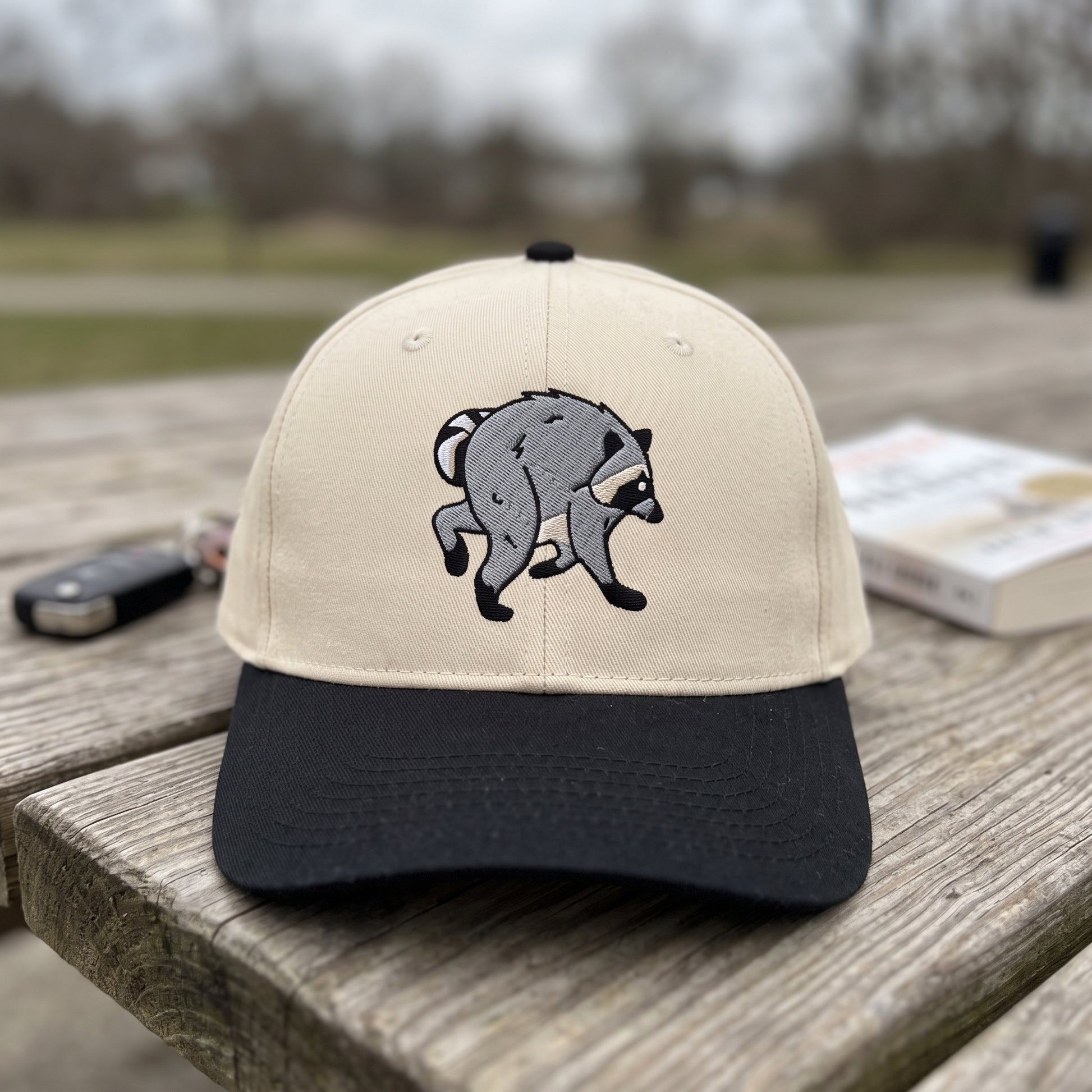 Jimothy Raccoon embroidered hat in Black/natural resting on a flat surface