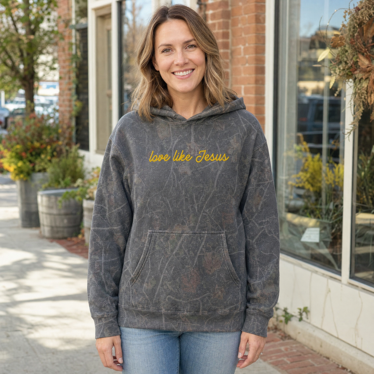 Model wearing the Love Like Jesus heavyweight hoodie in Dark Tree Camo, cover image 1