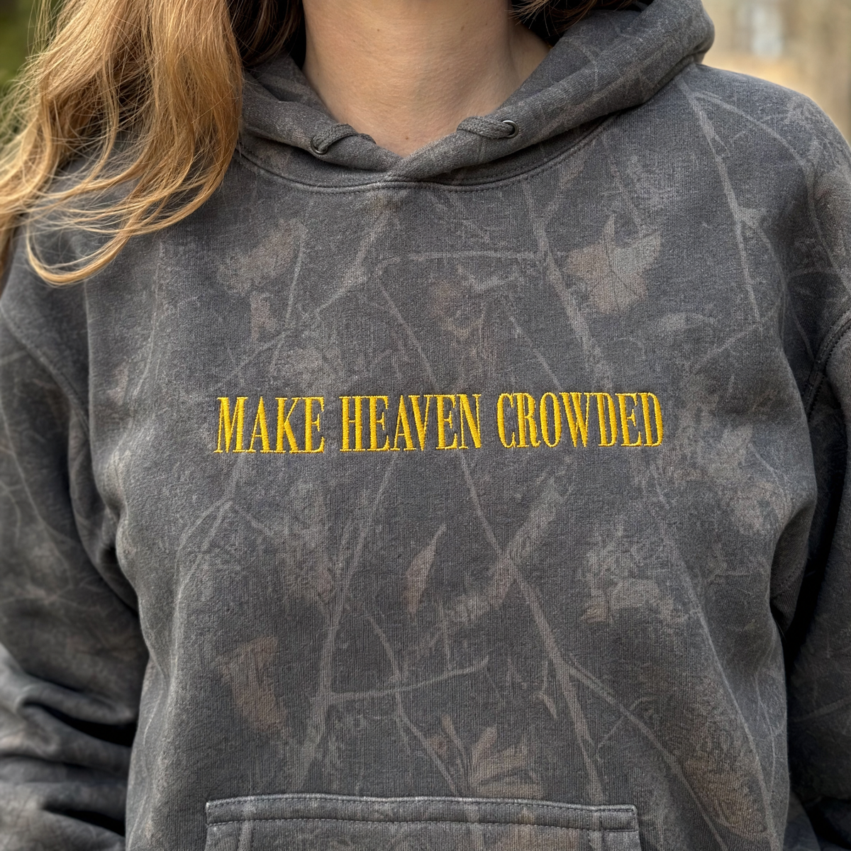Model wearing the Make Heaven Crowded heavyweight hoodie in Dark Tree Camo, lifestyle image 1