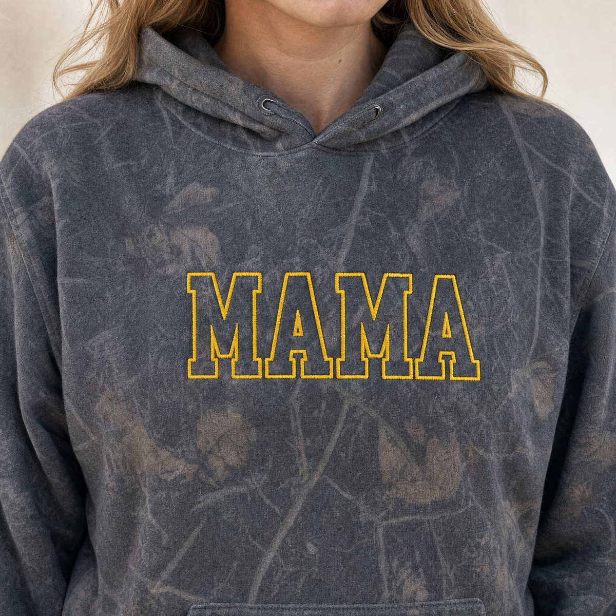 Model wearing the Mama Outline Text heavyweight hoodie in Dark Tree Camo, lifestyle image 1