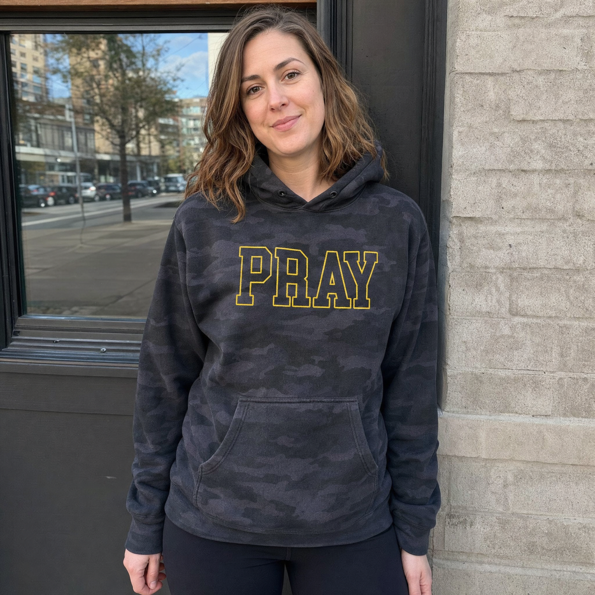 Model wearing the Pray Outline Text heavyweight hoodie in Black Camo, lifestyle image 1