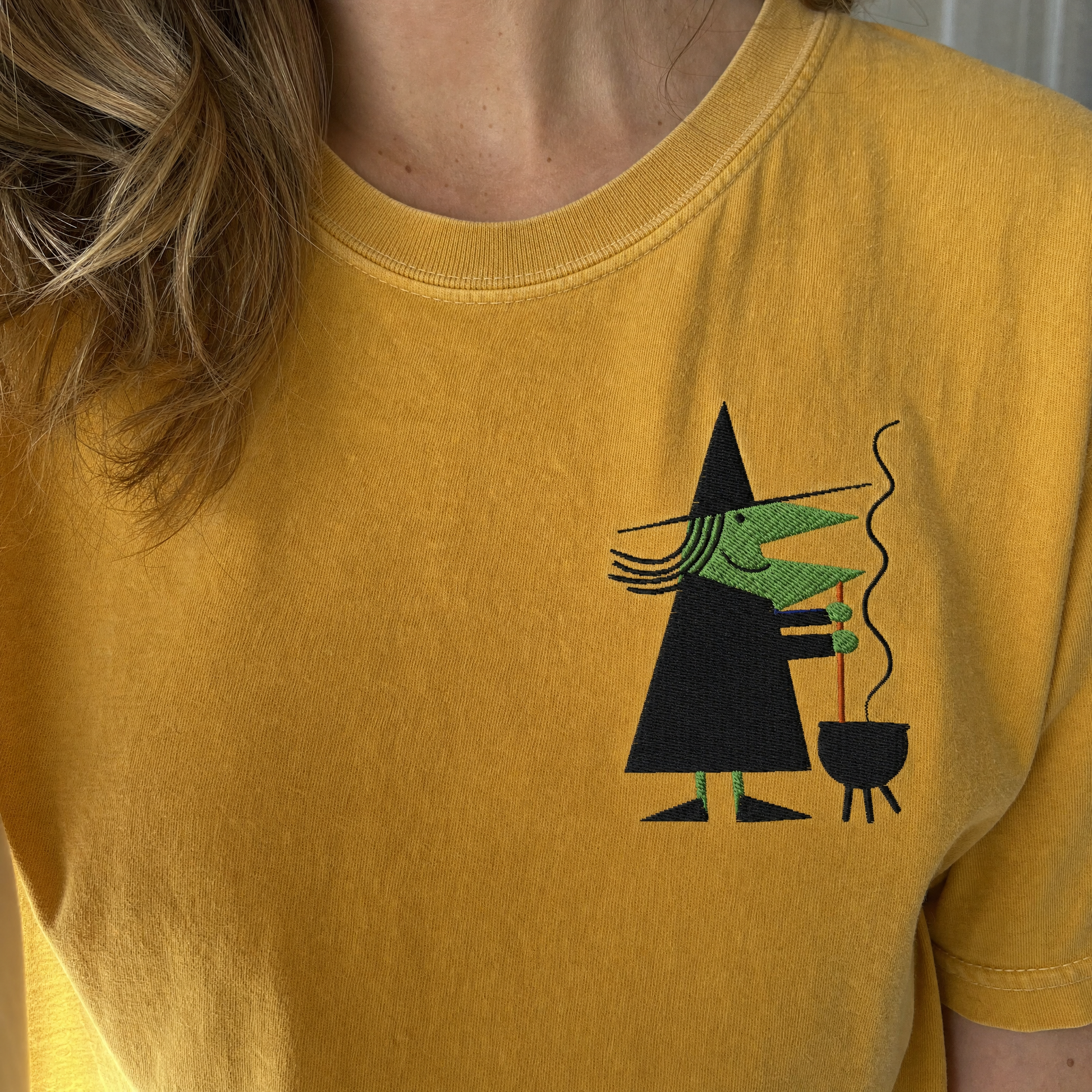 Model wearing the Retro Witch Stirring Cauldron comfort colors tee in Mustard, lifestyle image 1