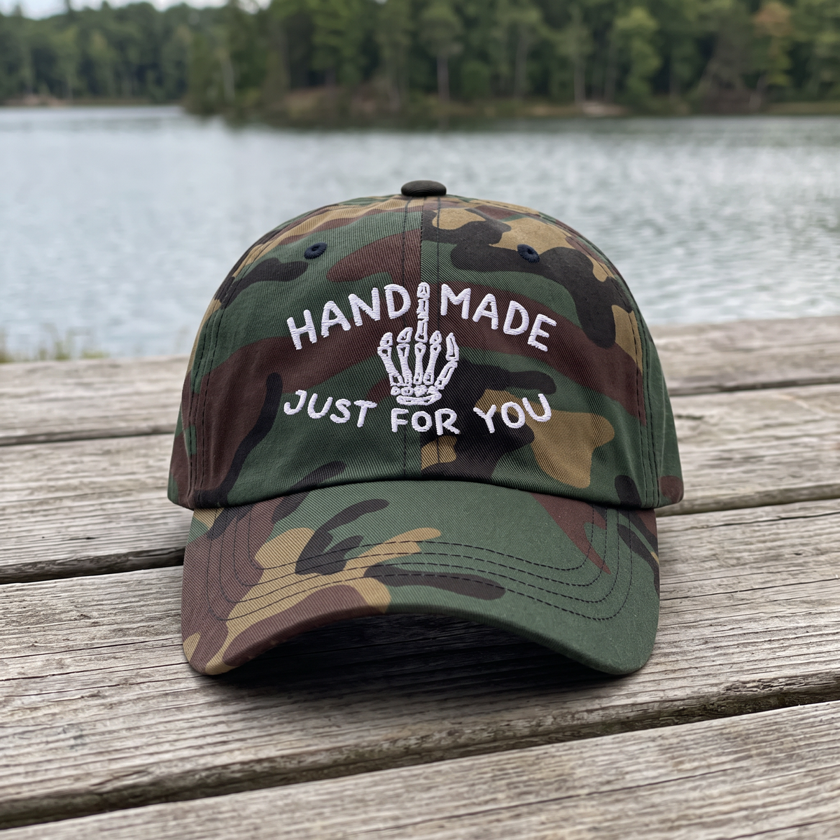 Skeleton Middle Finger embroidered hat in Green Camo resting on a flat surface, lifestyle image 1