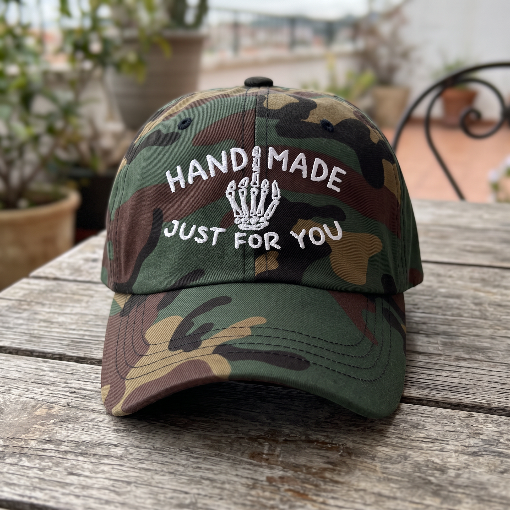 Skeleton Middle Finger embroidered hat in Green Camo resting on a flat surface, lifestyle image 2