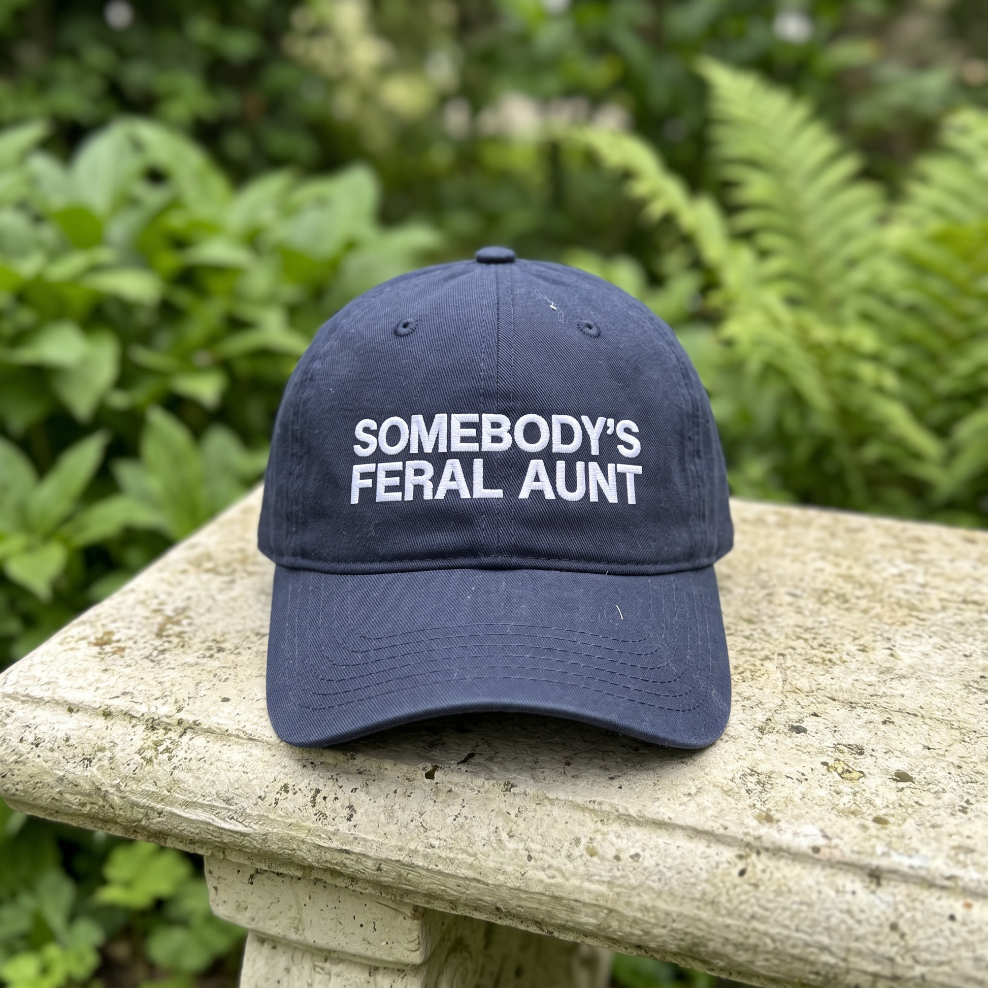 Somebody's Feral Aunt embroidered hat in Navy resting on a flat surface, lifestyle image 2