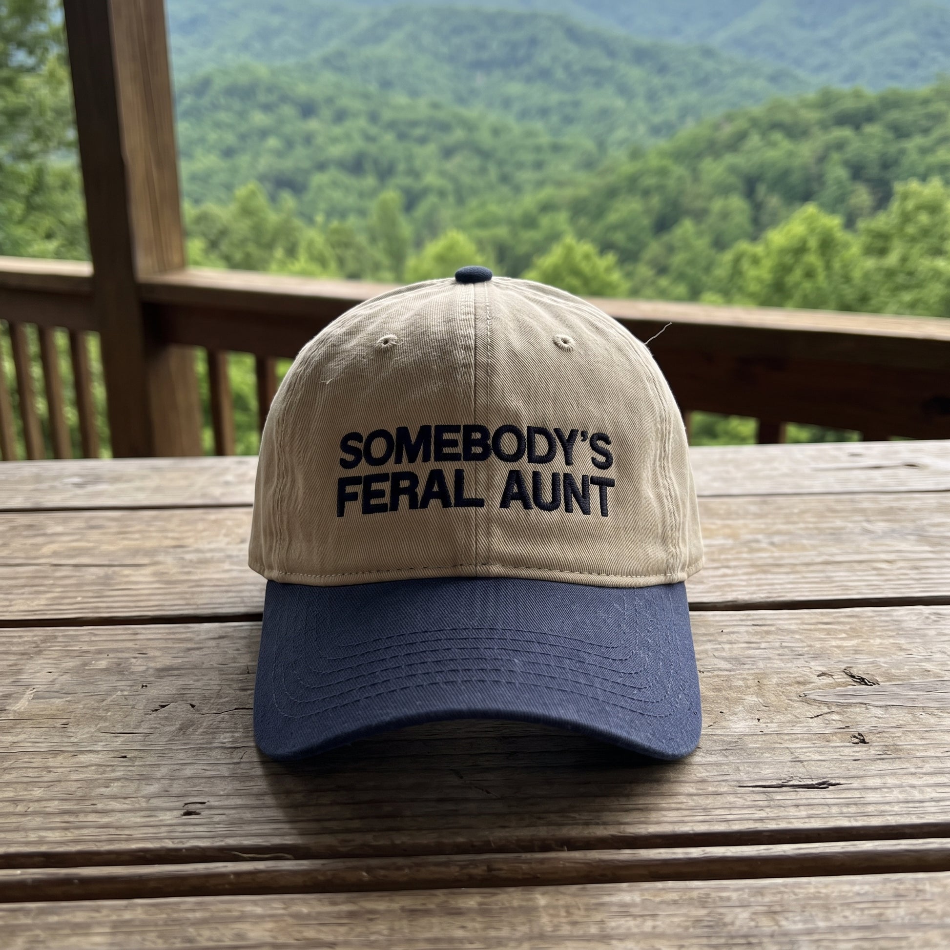 Somebody's Feral Aunt embroidered hat in Navy/khaki resting on a flat surface, lifestyle image 1