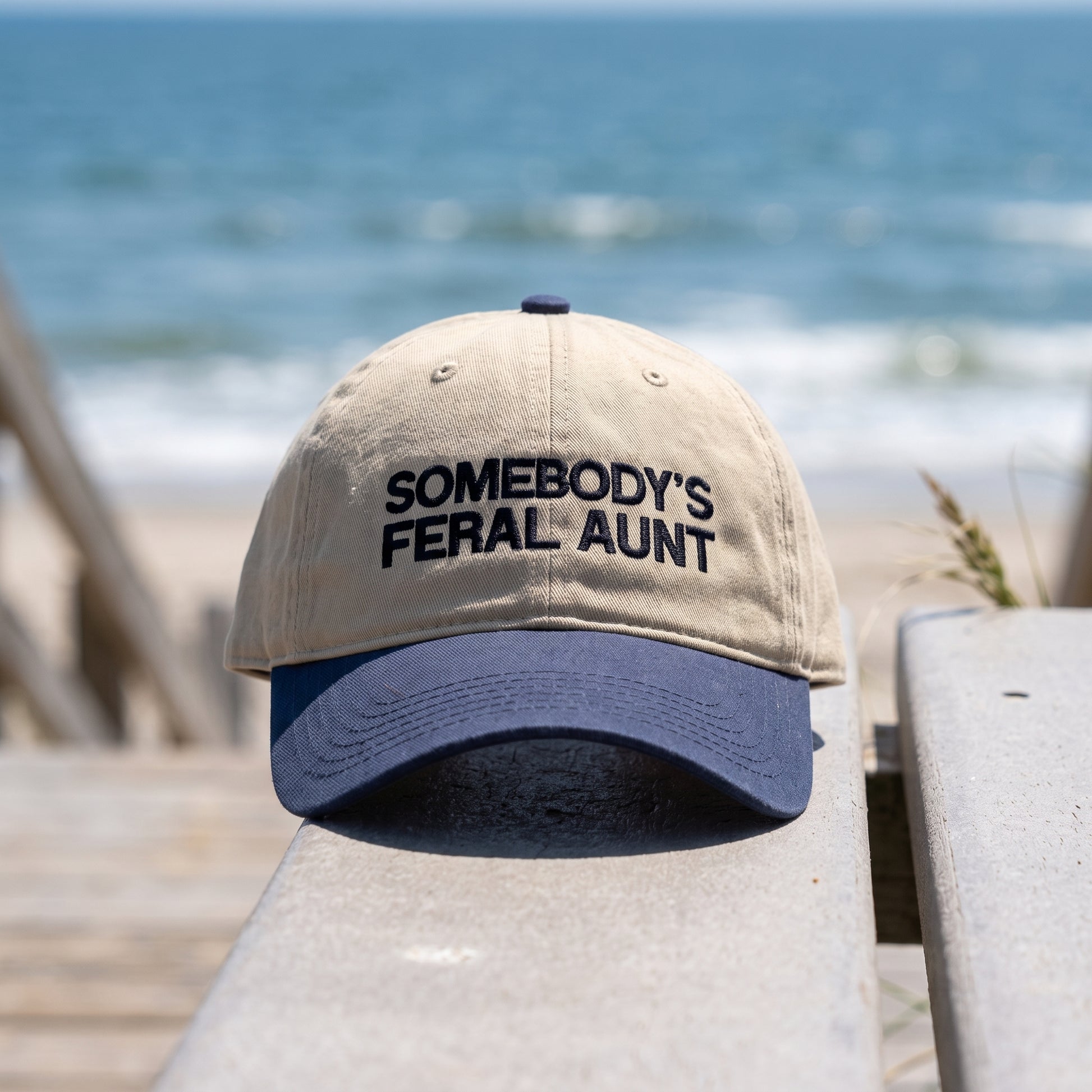 Somebody's Feral Aunt embroidered hat in Navy/khaki resting on a flat surface, lifestyle image 2