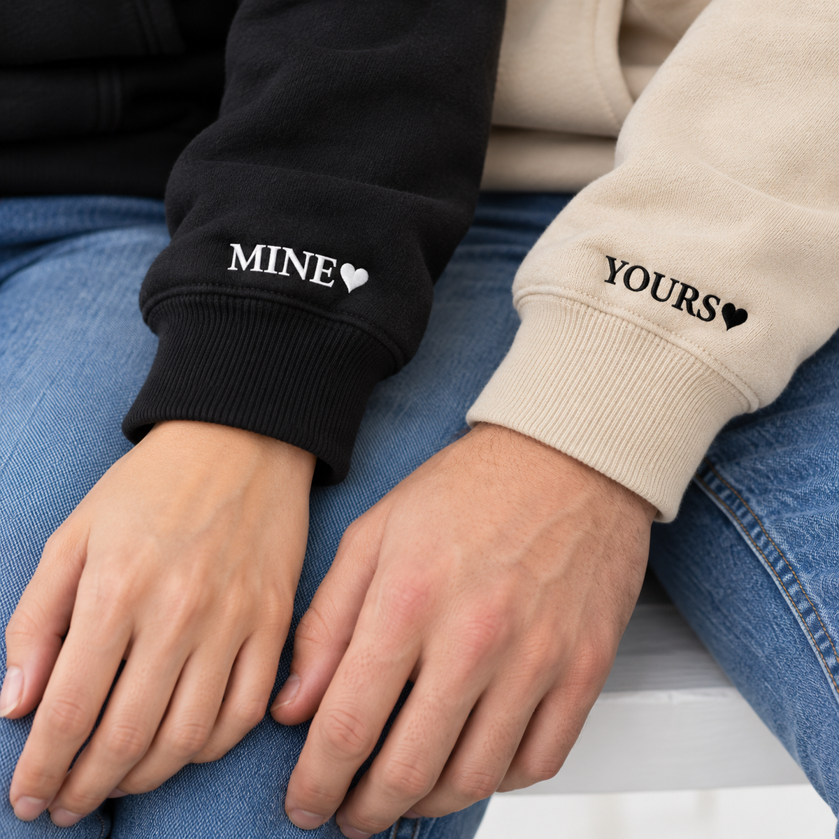 Lifestyle close-up of MINE and YOURS with aligned hearts on Black and Sand hoodie sleeves.