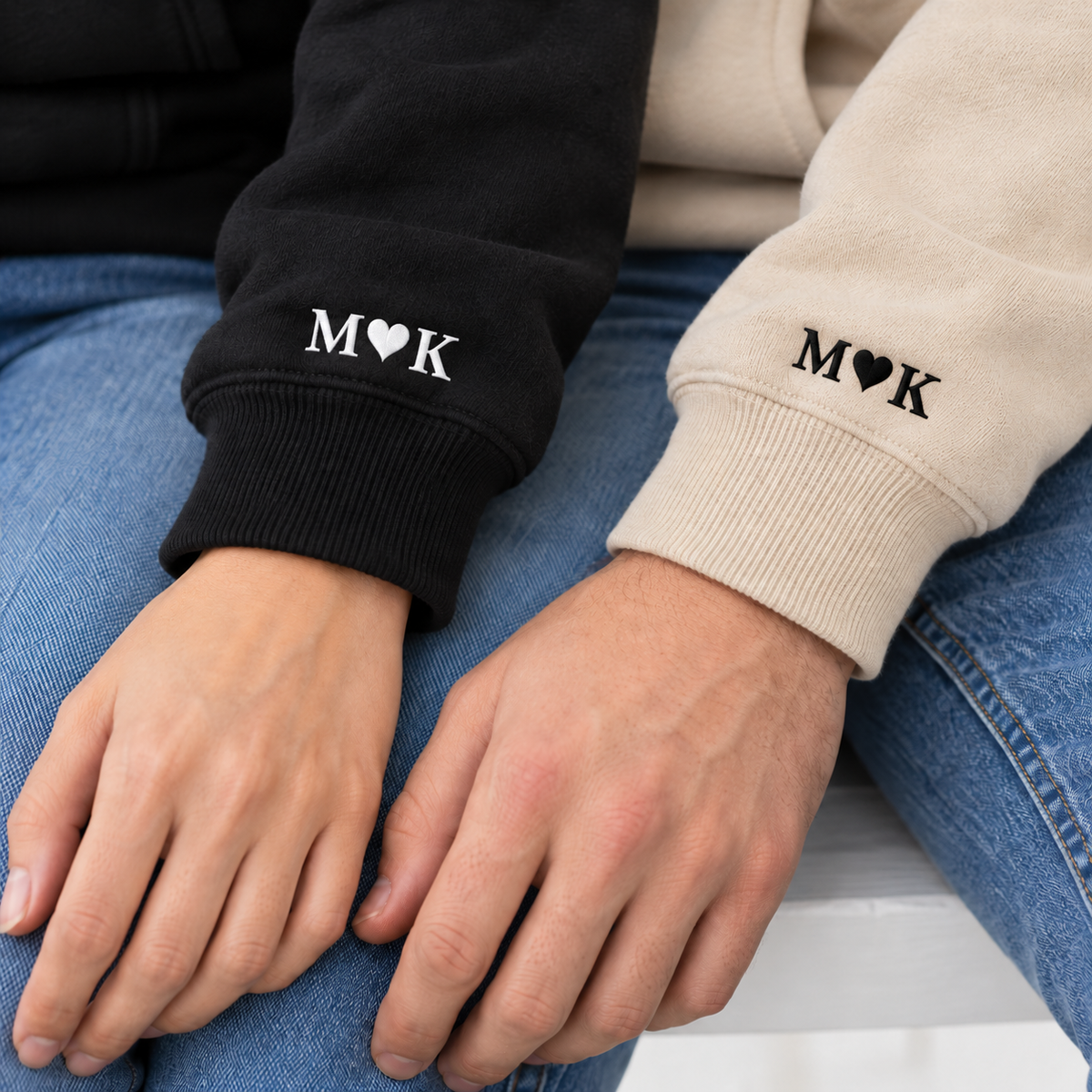 Lifestyle close-up of M heart K embroidery on Black and Sand hoodie sleeves.